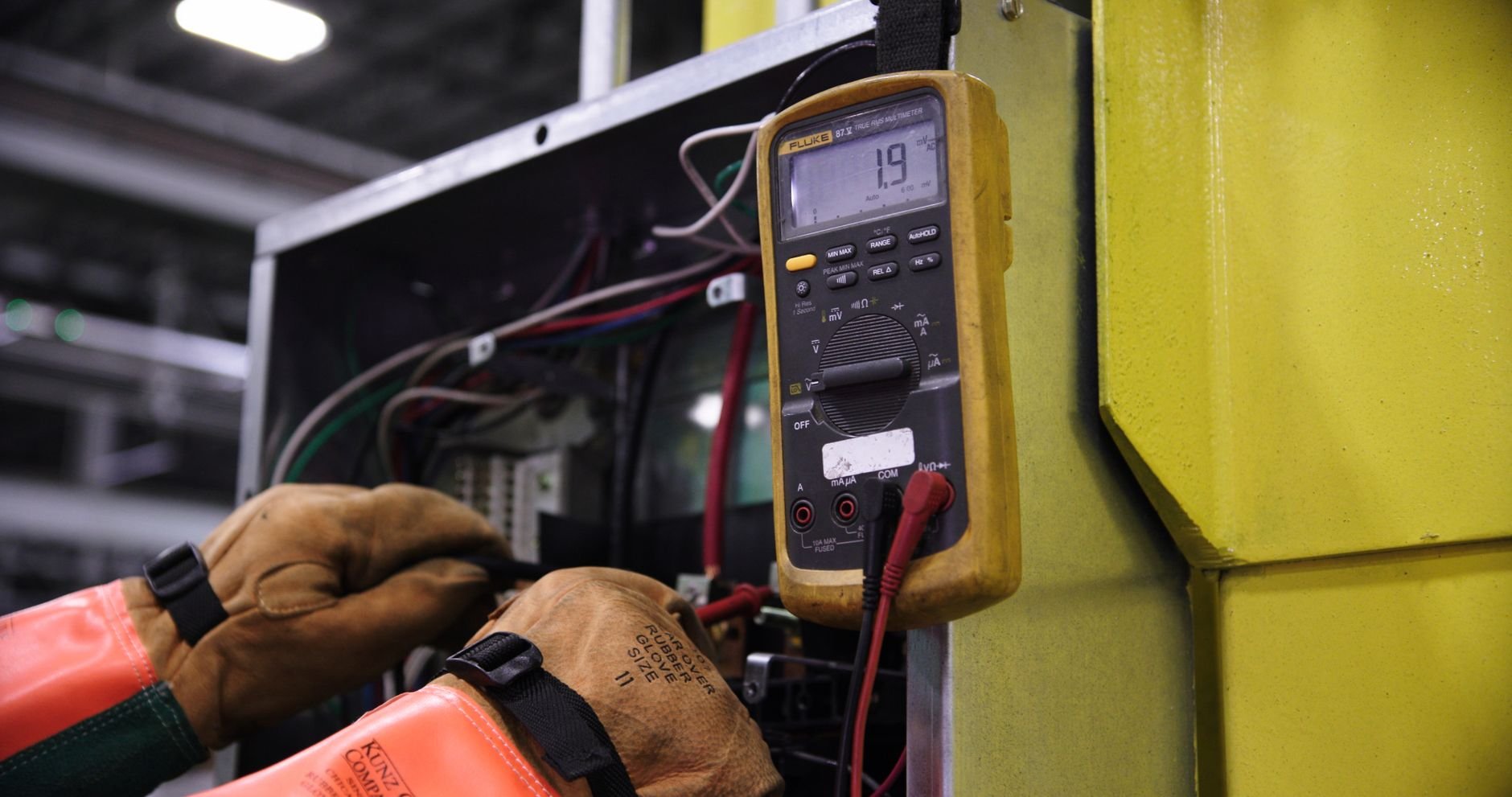 Electrician using a multimeter to fix industrial control panel wiring